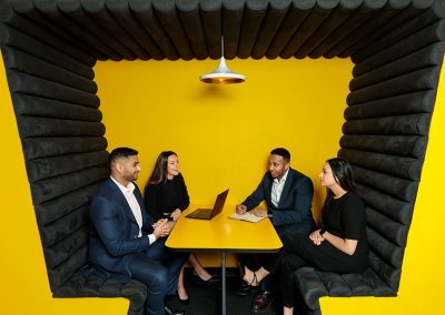 Four business workers sit in a yellow office booth discussing corporate strategy