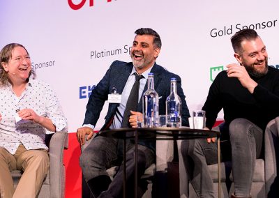 Three men laughing during a conference presentation on a corporate stage