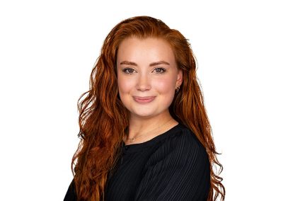A corporate headshot of a young business woman with ginger hair smiles at the camera