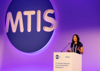 A corporate woman is dwarfed but a large business logo on stage at a London conference