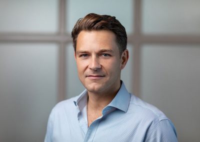 A confident man in a business shirt looks directly into the camera capturing his headshot