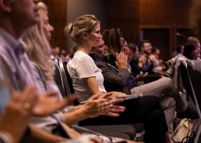 A woman in the middle of a conference audience listens carefully to a business speaker