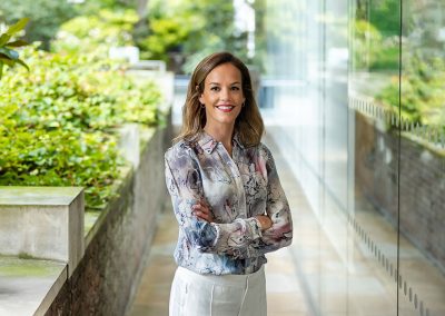 A smart corporate lady poses outside a London office surrounded by greenery and glass