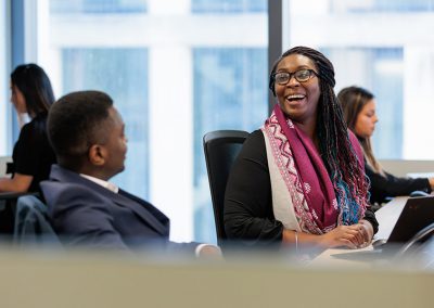 A young black business lady laugh whilst sitting at her desk talking to a colleague